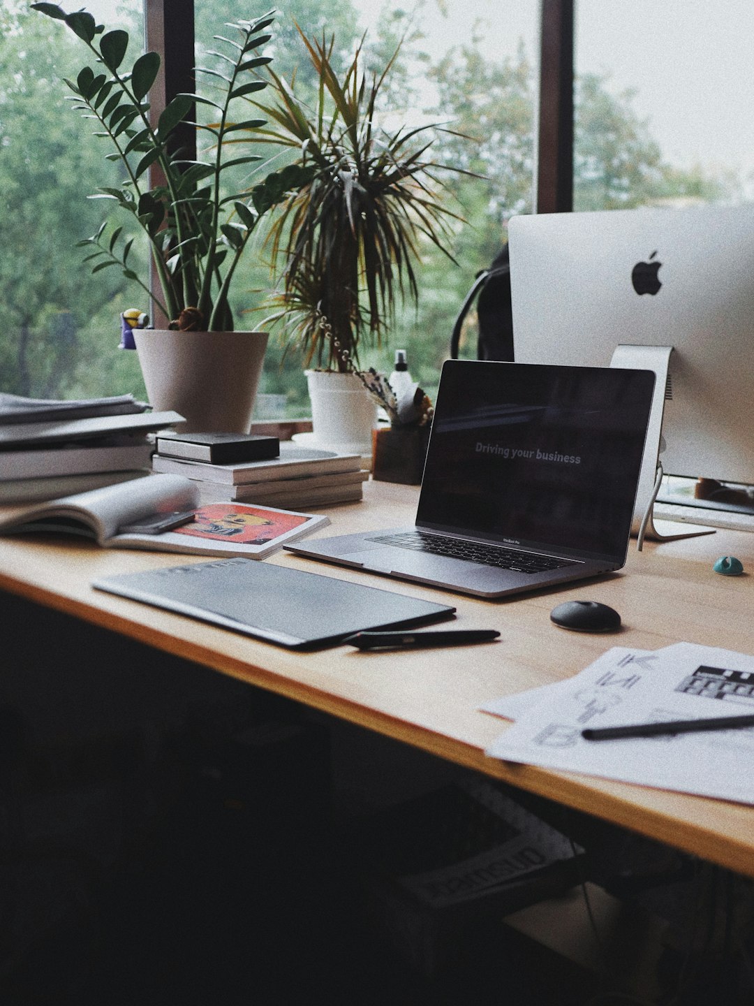 A maker's desk with a laptop, notebooks, and plants